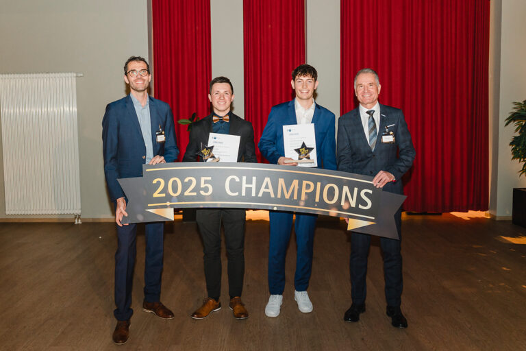 Vier Personen posieren mit einer Auszeichnung für die 2025 Champions in einem Innenraum.