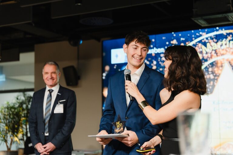 Julian Schleager in einem blauen Anzug, während er auf einer Bühne eine Auszeichnung erhält.