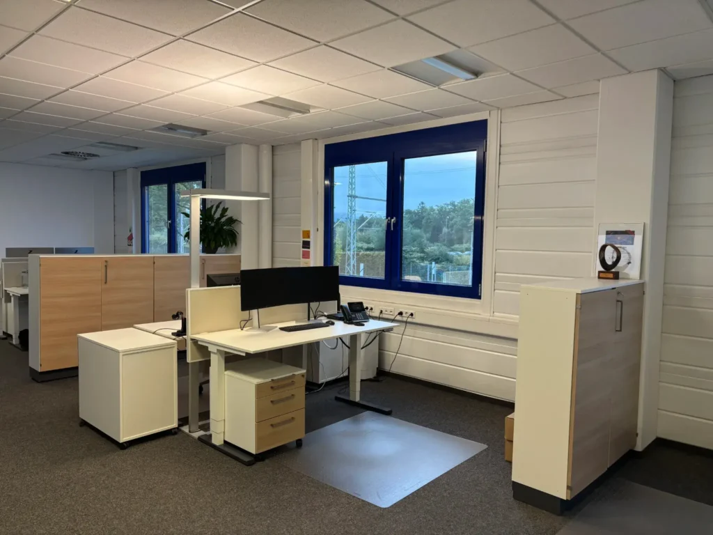 Moderne Büroumgebung mit Schreibtisch, Computer und hellen Fenstern in einem Arbeitsbereich.